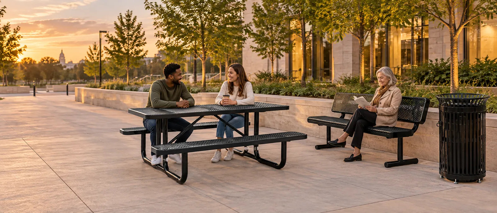 Illustration: a black expanded metal picnic table, a bench with backrest and a slatted steel receptacle in use on a landscaped civic plaza.